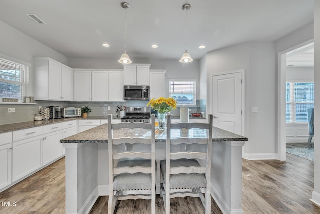 kitchen featuring decorative light fixtures, stainless steel appliances, stone counters, and an island with sink