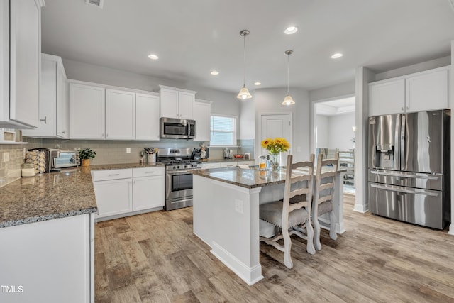 kitchen featuring white cabinetry, a center island, dark stone counters, pendant lighting, and appliances with stainless steel finishes