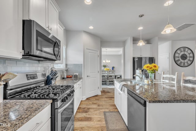 kitchen featuring decorative backsplash, stainless steel appliances, decorative light fixtures, a center island with sink, and white cabinetry