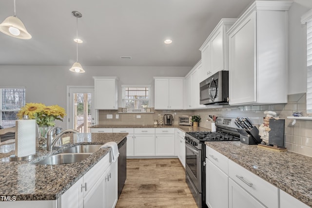 kitchen with white cabinets, pendant lighting, appliances with stainless steel finishes, and dark stone counters