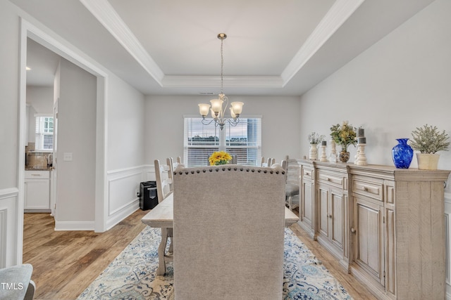 dining space with a raised ceiling, ornamental molding, light wood-type flooring, and an inviting chandelier