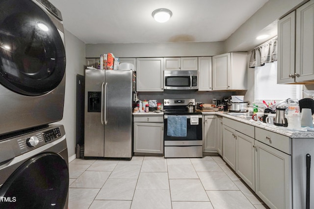 kitchen with appliances with stainless steel finishes, gray cabinets, light tile patterned floors, and stacked washer and clothes dryer