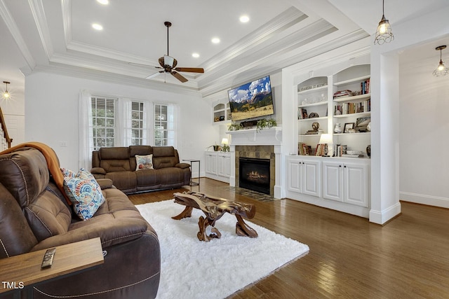 living room with built in shelves, ceiling fan, a tile fireplace, dark hardwood / wood-style flooring, and ornamental molding