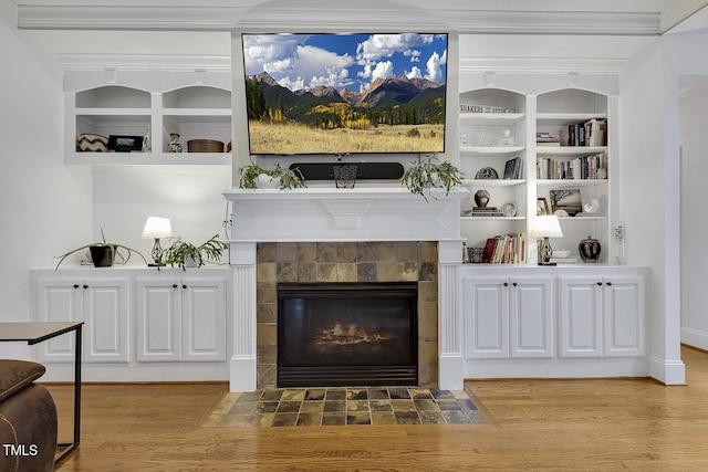 interior space featuring a tile fireplace, built in shelves, hardwood / wood-style flooring, and crown molding