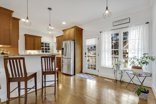 kitchen with a kitchen bar, stainless steel fridge, light stone counters, and decorative light fixtures