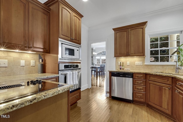 kitchen with sink, light wood-type flooring, ornamental molding, appliances with stainless steel finishes, and light stone counters