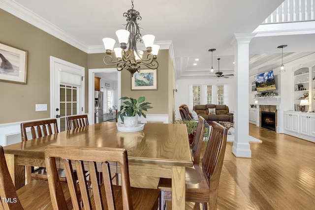 dining room featuring decorative columns, ornamental molding, built in shelves, ceiling fan with notable chandelier, and hardwood / wood-style flooring