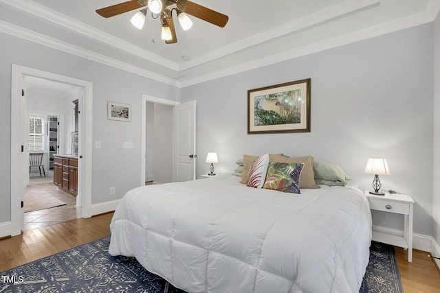 bedroom featuring ensuite bath, ornamental molding, a tray ceiling, ceiling fan, and wood-type flooring