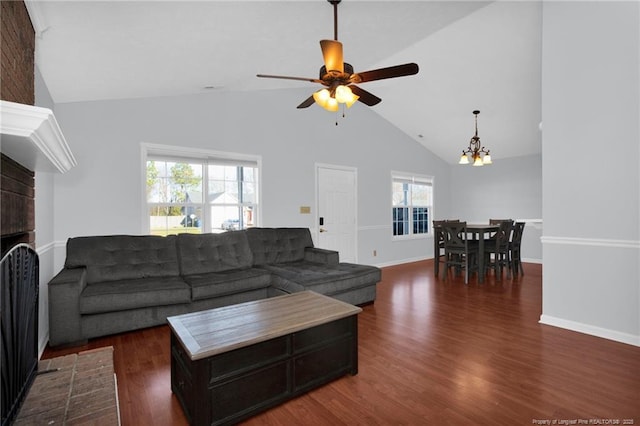 living room featuring ceiling fan with notable chandelier, dark hardwood / wood-style flooring, vaulted ceiling, and a fireplace