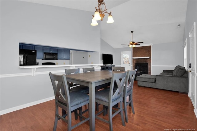 dining space featuring ceiling fan with notable chandelier, dark hardwood / wood-style flooring, high vaulted ceiling, and a brick fireplace