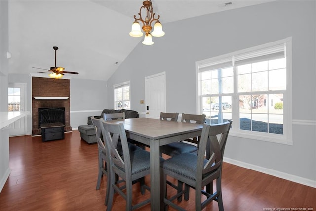 dining room with a fireplace, ceiling fan with notable chandelier, dark hardwood / wood-style floors, and high vaulted ceiling