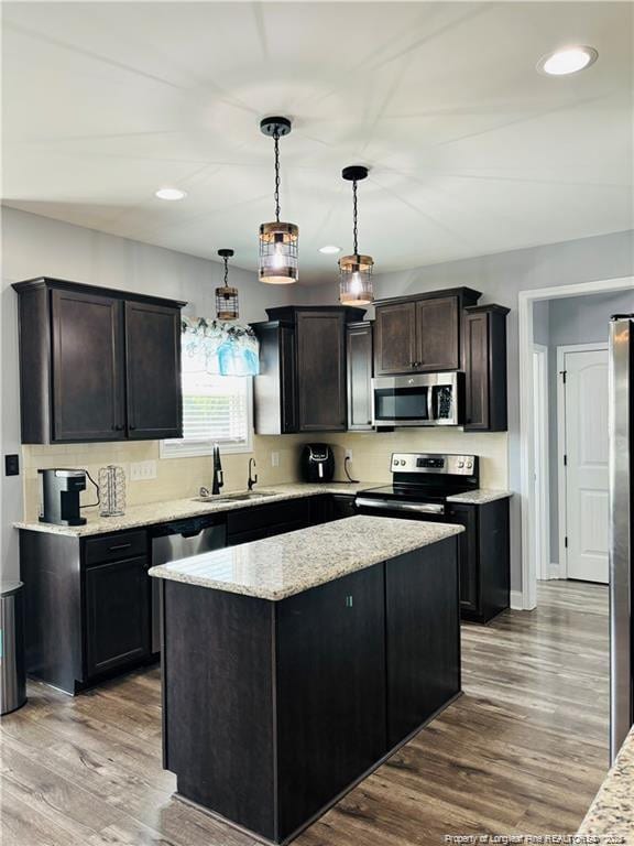 kitchen with appliances with stainless steel finishes, a kitchen island, pendant lighting, and hardwood / wood-style floors