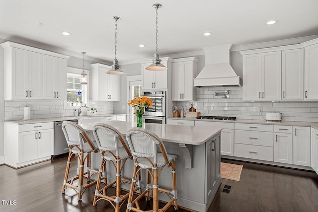 kitchen with appliances with stainless steel finishes, white cabinetry, a center island, and custom range hood