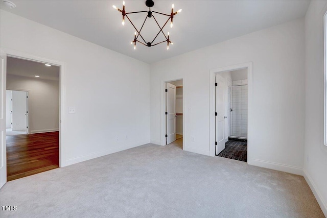 unfurnished bedroom featuring an inviting chandelier, ensuite bathroom, a spacious closet, light colored carpet, and a closet