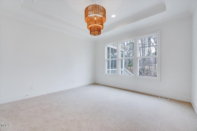 spare room with carpet floors, a raised ceiling, and a notable chandelier