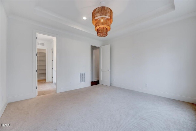 unfurnished bedroom featuring light carpet, a raised ceiling, a walk in closet, ornamental molding, and a closet