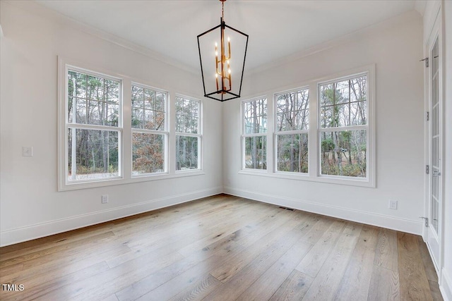 unfurnished dining area featuring light hardwood / wood-style floors, ornamental molding, and an inviting chandelier