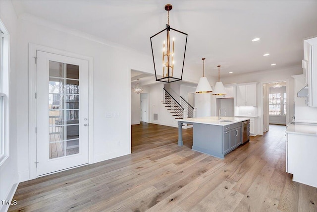 kitchen featuring a kitchen island with sink, crown molding, sink, white cabinetry, and hanging light fixtures