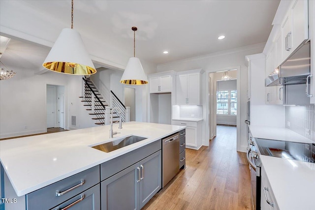 kitchen with stainless steel appliances, a kitchen island with sink, sink, pendant lighting, and white cabinetry