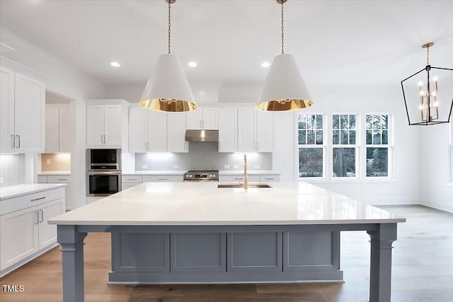 kitchen featuring a large island with sink, white cabinets, sink, decorative backsplash, and appliances with stainless steel finishes