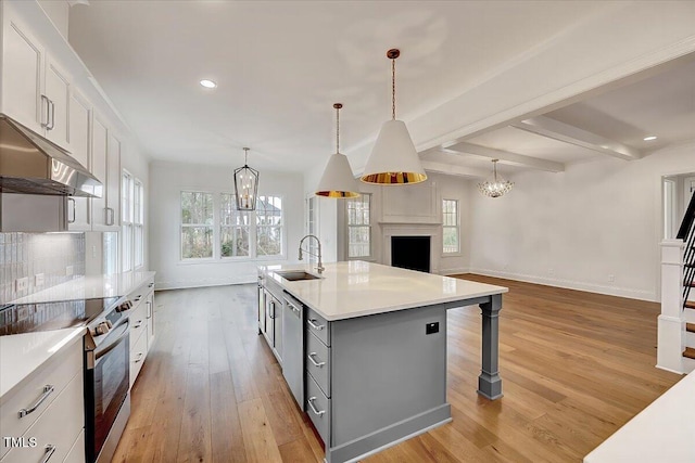 kitchen with white cabinets, stainless steel appliances, hanging light fixtures, and an island with sink