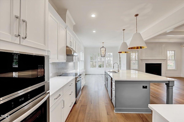 kitchen featuring a kitchen island with sink, hanging light fixtures, sink, white cabinetry, and stainless steel appliances