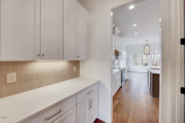 kitchen featuring decorative backsplash, light wood-type flooring, electric range, an inviting chandelier, and white cabinetry