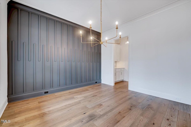 unfurnished dining area with light wood-type flooring, ornamental molding, and a notable chandelier