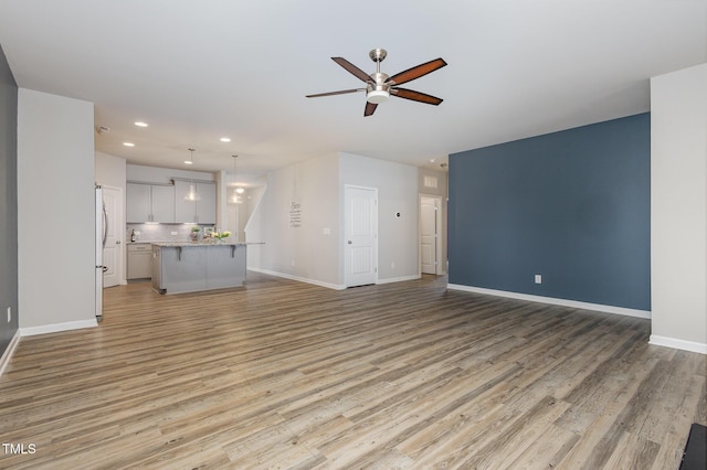 unfurnished living room featuring ceiling fan and light wood-type flooring