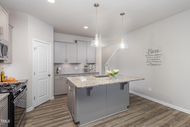 kitchen with sink, a kitchen island with sink, light stone counters, and black gas range