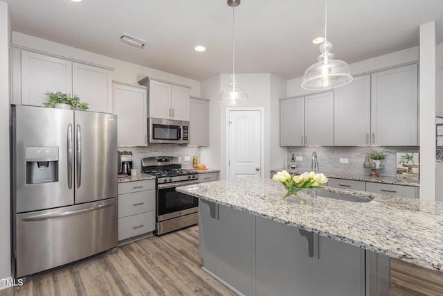 kitchen with light stone counters, pendant lighting, stainless steel appliances, and a kitchen bar