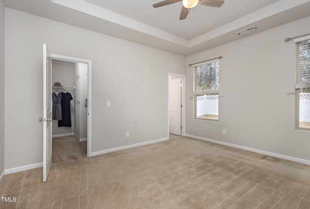 unfurnished bedroom featuring a raised ceiling, a spacious closet, light carpet, and a closet