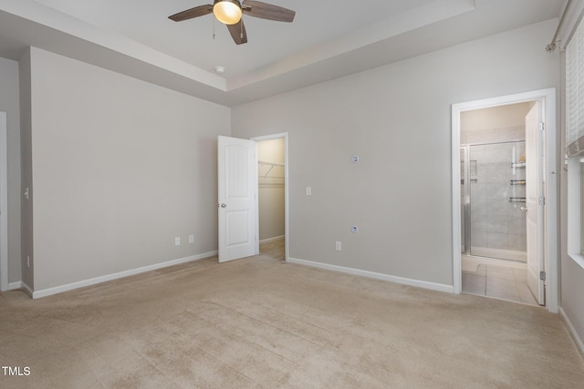 unfurnished bedroom with ensuite bath, a walk in closet, a tray ceiling, a closet, and light colored carpet