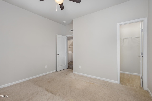 unfurnished bedroom featuring ceiling fan, washer / dryer, light carpet, a spacious closet, and a closet