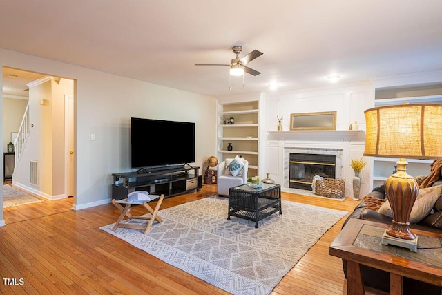 living room featuring a fireplace, built in shelves, ceiling fan, and hardwood / wood-style floors