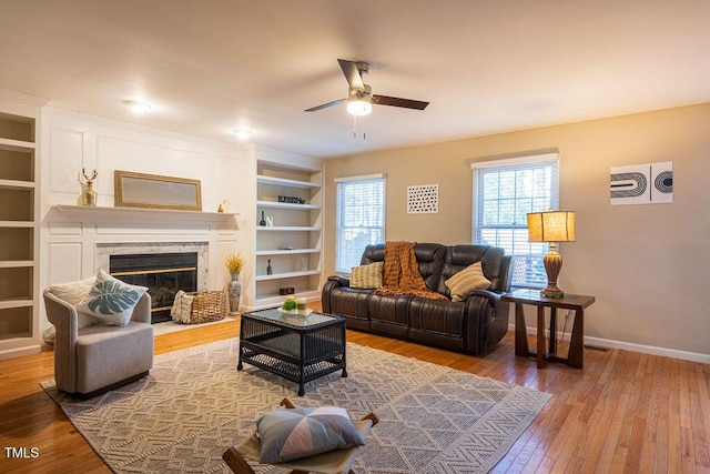 living room featuring built in shelves, a premium fireplace, ceiling fan, and wood-type flooring