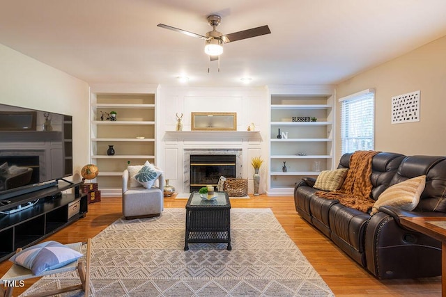 living room featuring a high end fireplace, light wood-type flooring, built in features, and ceiling fan