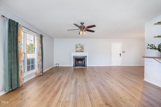 unfurnished living room featuring ceiling fan, a premium fireplace, a textured ceiling, and light hardwood / wood-style flooring