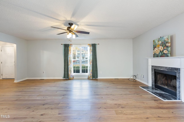 unfurnished living room featuring a fireplace, a textured ceiling, light wood-type flooring, and ceiling fan