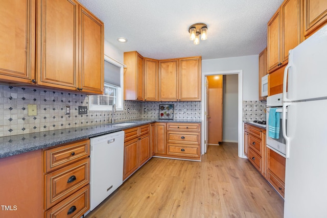 kitchen with white appliances, decorative backsplash, dark stone countertops, light wood-type flooring, and a textured ceiling