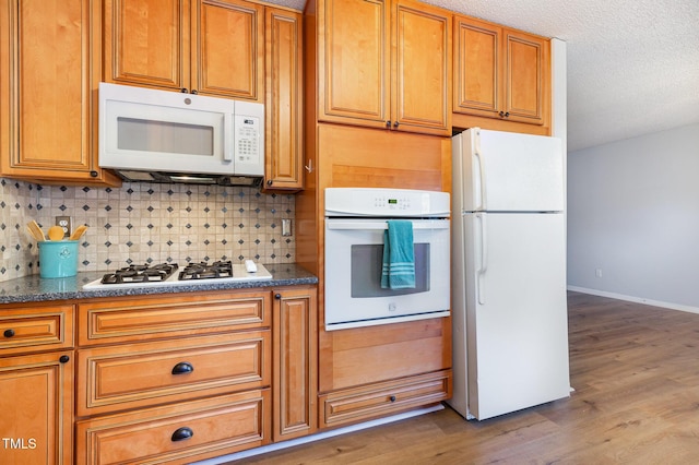 kitchen with hardwood / wood-style floors, white appliances, tasteful backsplash, and a textured ceiling