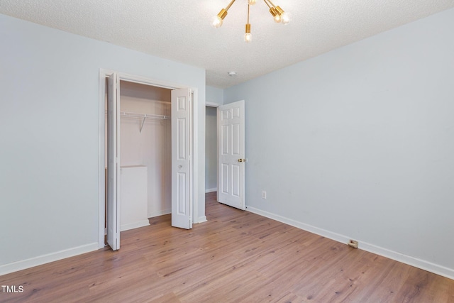 unfurnished bedroom featuring a textured ceiling, a notable chandelier, light hardwood / wood-style flooring, and a closet