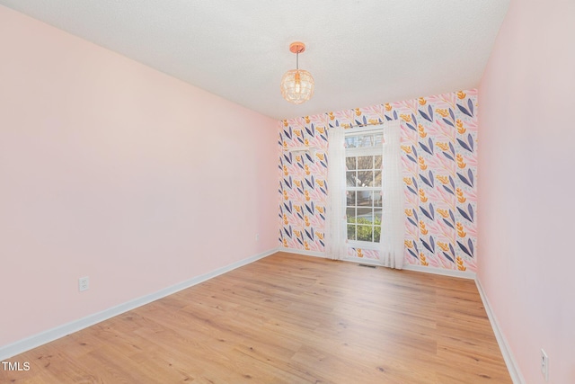 spare room with light hardwood / wood-style floors, a textured ceiling, and a chandelier