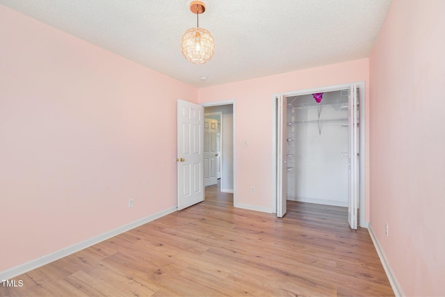 unfurnished bedroom with a textured ceiling, light wood-type flooring, a closet, and a notable chandelier