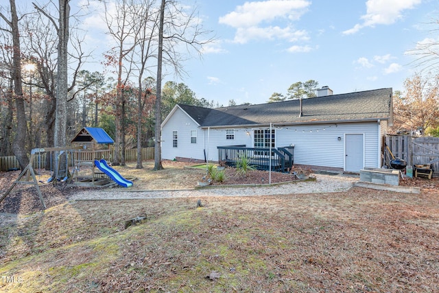 rear view of property featuring a playground and a wooden deck