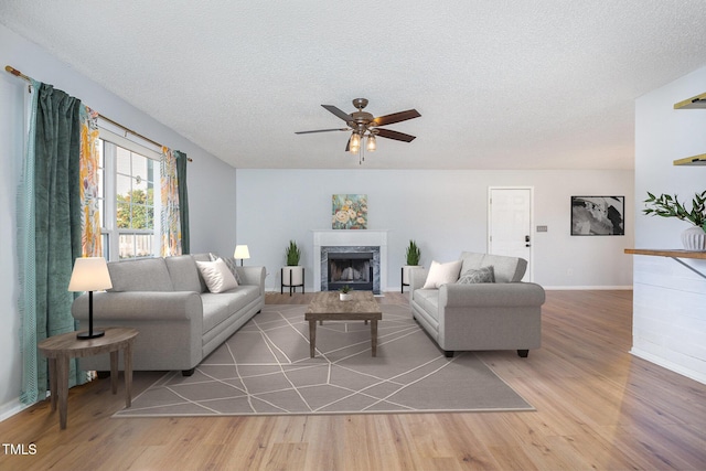 living room featuring ceiling fan, wood-type flooring, a textured ceiling, and a premium fireplace