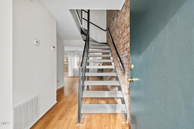 stairs with brick wall and hardwood / wood-style floors