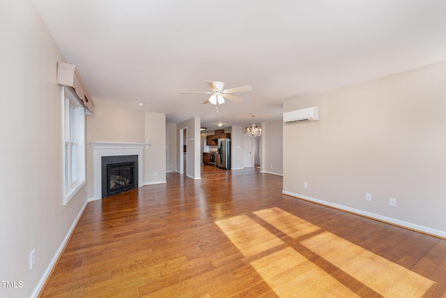 unfurnished living room featuring ceiling fan with notable chandelier, wood-type flooring, and an AC wall unit