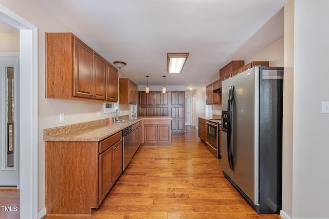 kitchen featuring light stone countertops, appliances with stainless steel finishes, sink, pendant lighting, and light hardwood / wood-style floors