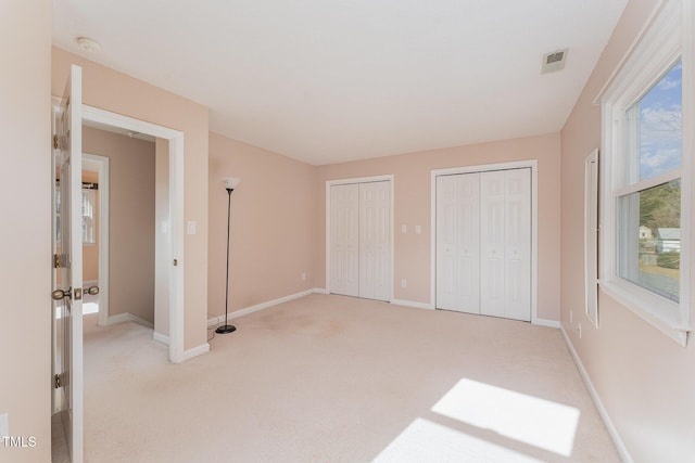 unfurnished bedroom featuring light carpet and two closets